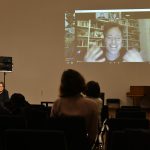 Rau (on screen) speaking, with the audience in the foreground