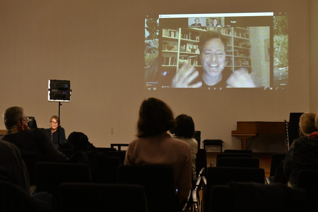 Rau (on screen) speaking, with the audience in the foreground