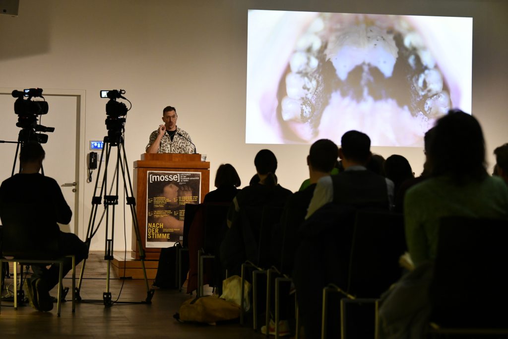 Hamdan delivering his lecture, with a slide in the background with a picture of an open mouth