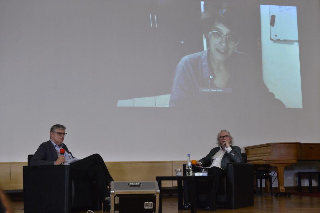 Nadim joins the conversation virtually. Her image is projected onscreen behind Tvedt and Müller