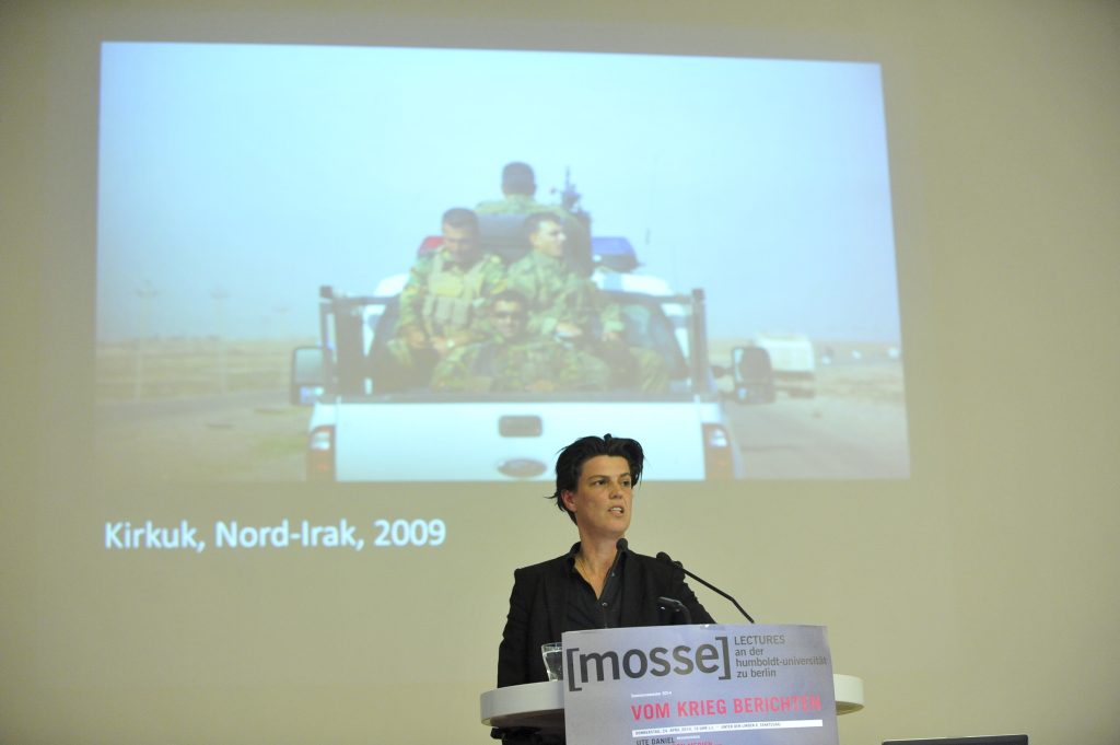 Emcke lectures from the podium, with photo in background