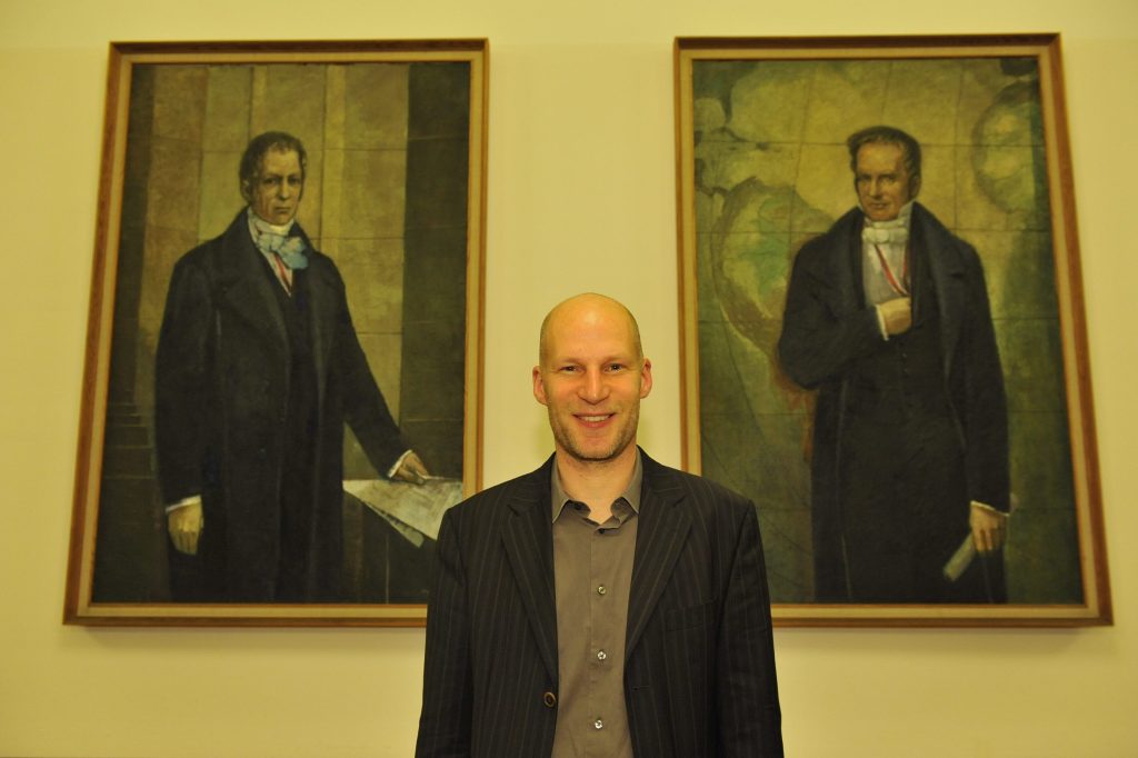Conrad poses in front of the portraits of the Humboldt brothers