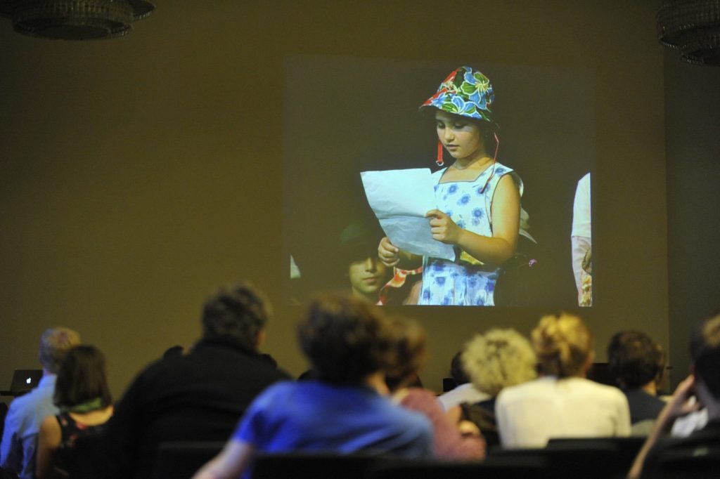 the audience looks on as footage is played