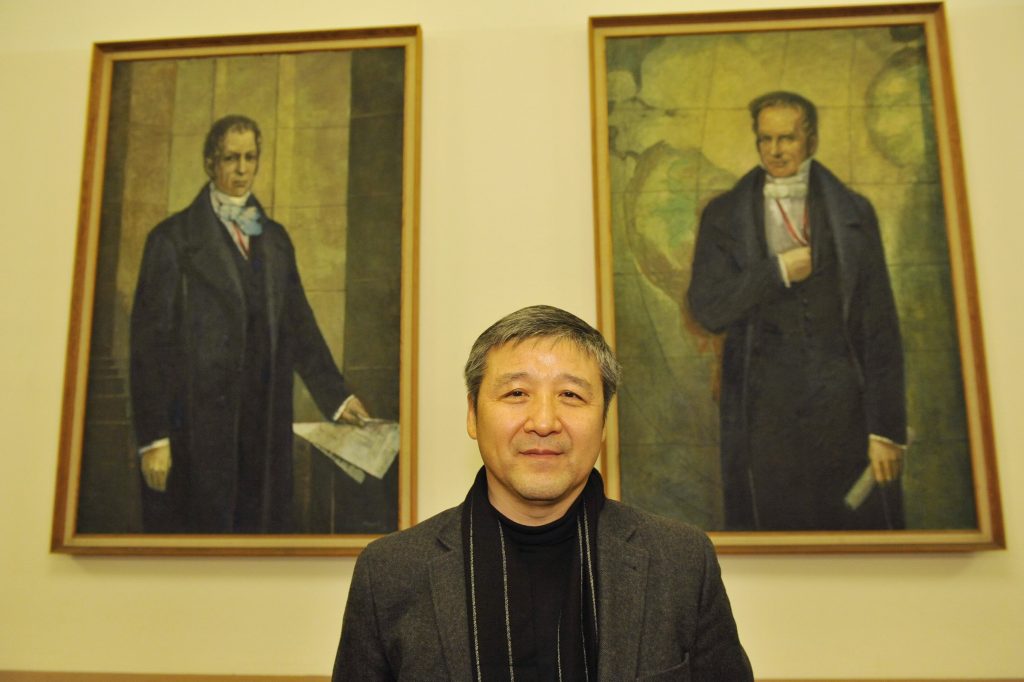 Hui poses before the portraits of the Humboldt brothers